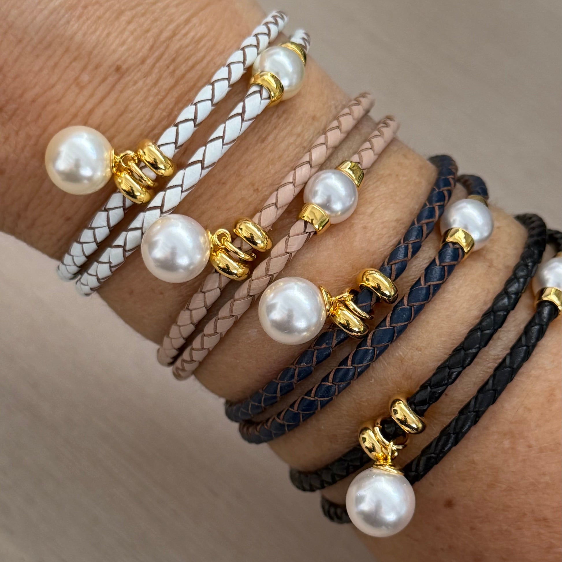 Multiple pearl-bride bracelets on a wrist against a neutral background