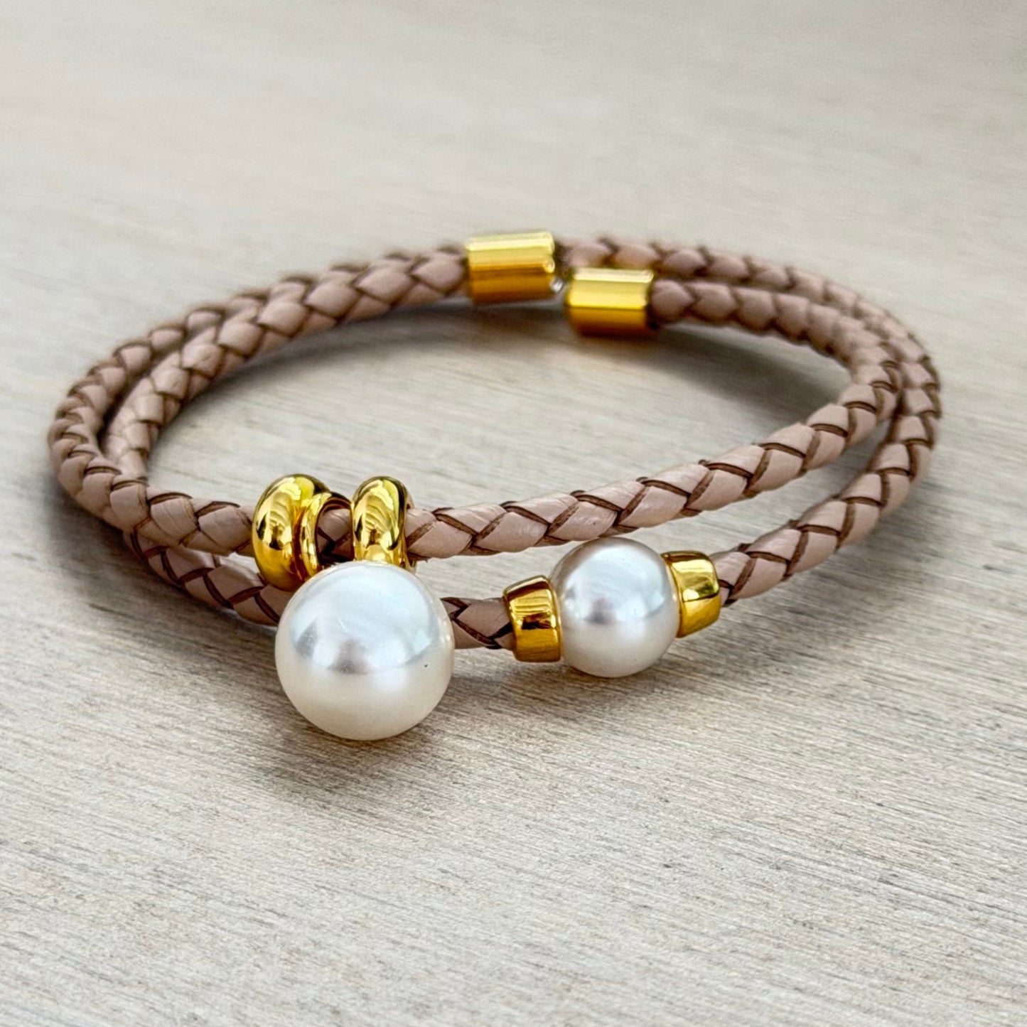 Brown braided leather bracelet with pearls and gold accents on a light gray background