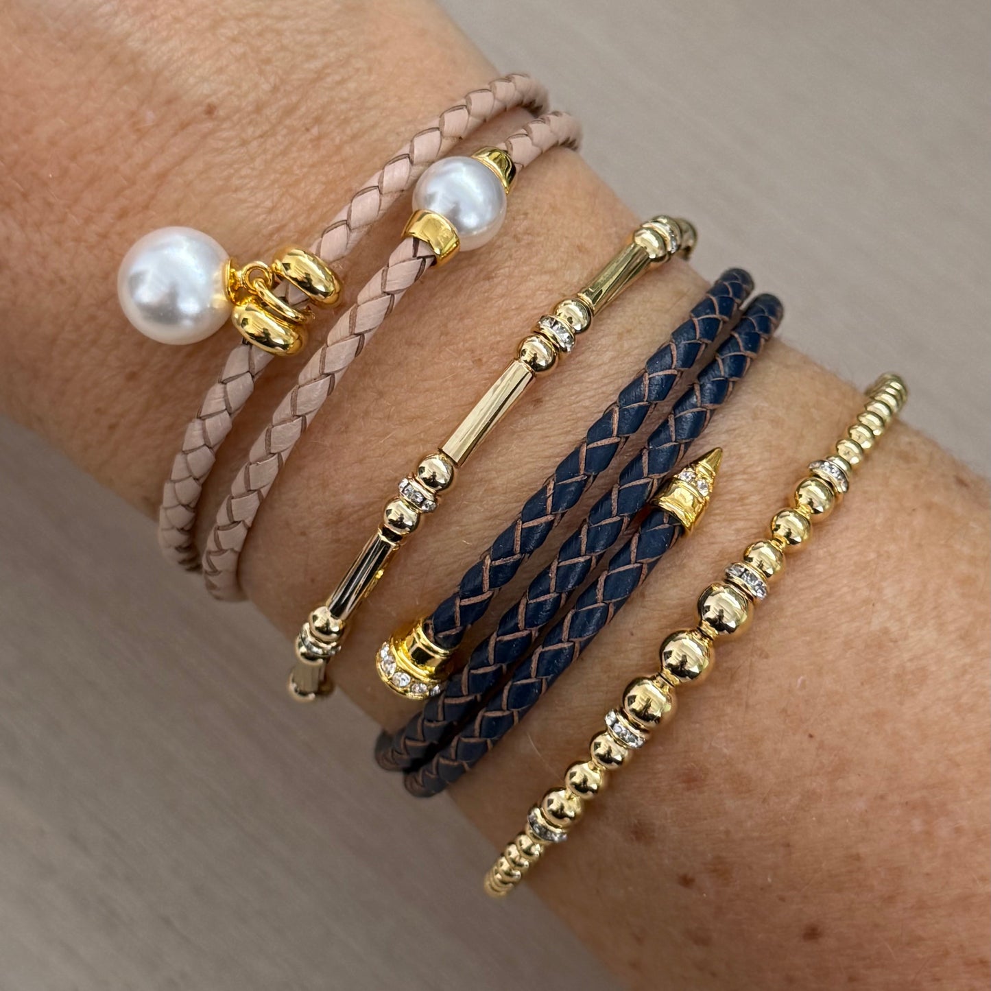 Close-up of a wrist wearing multiple bracelets with pearls and gold accents on a neutral background
