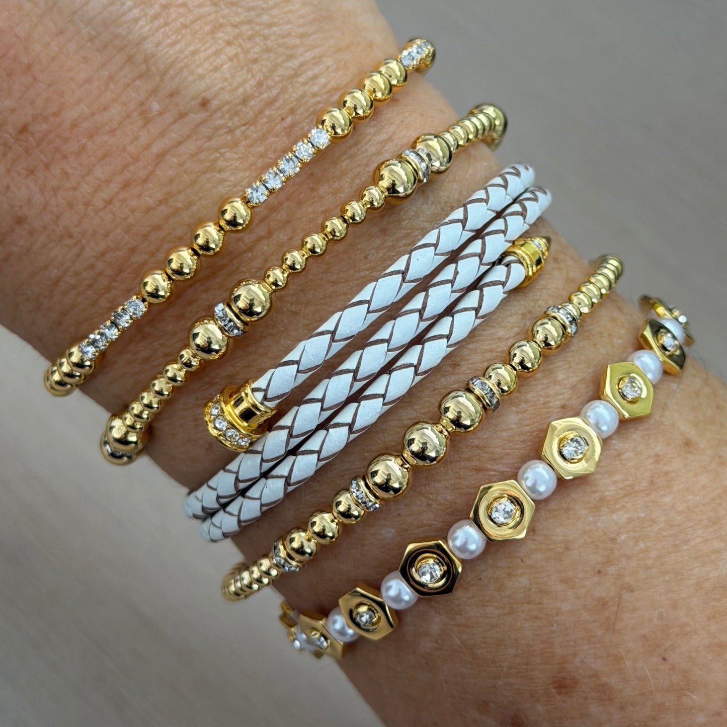 Multiple gold and white bracelets on a wrist against a neutral background