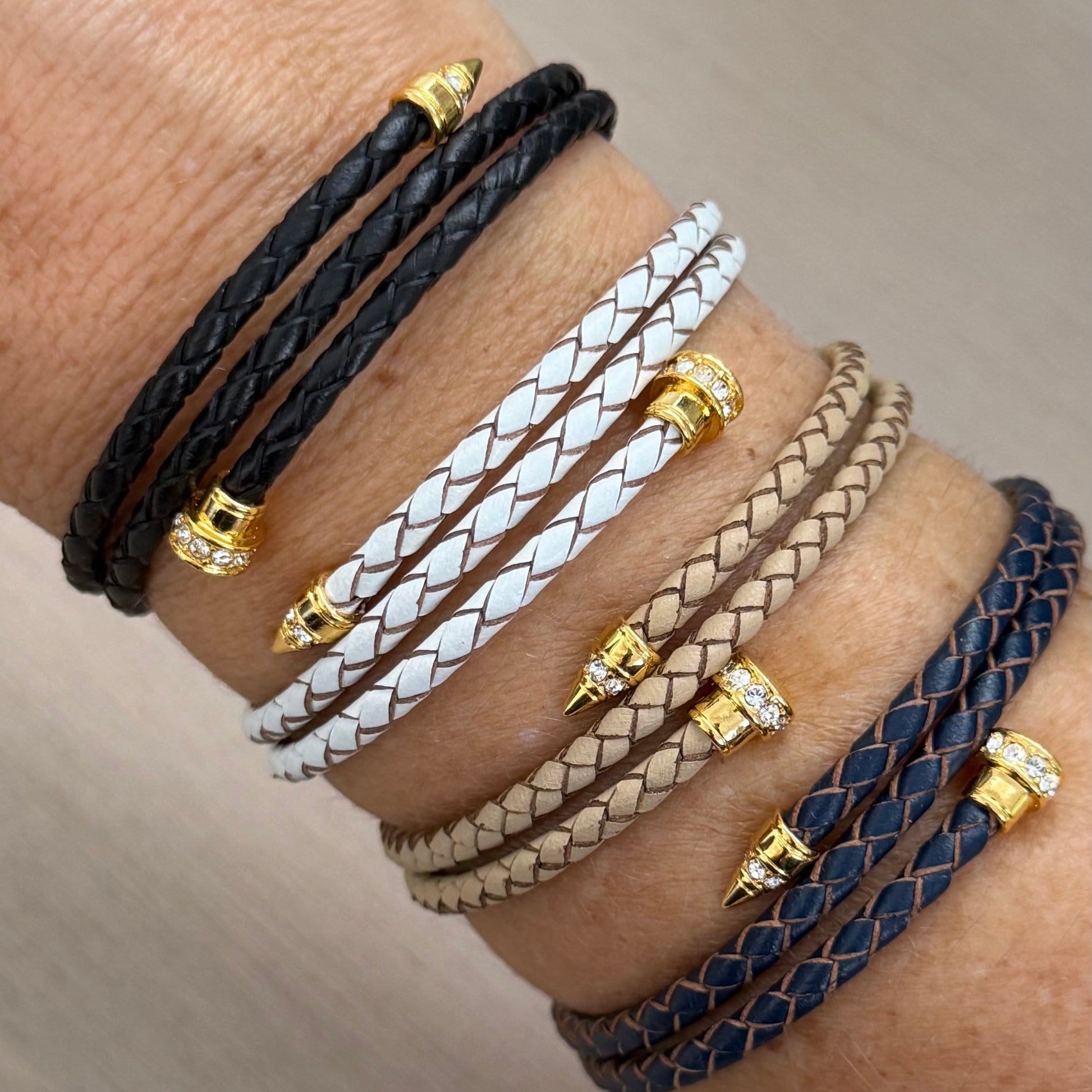 Multiple leather bracelets with gold accents on a wrist against a neutral background