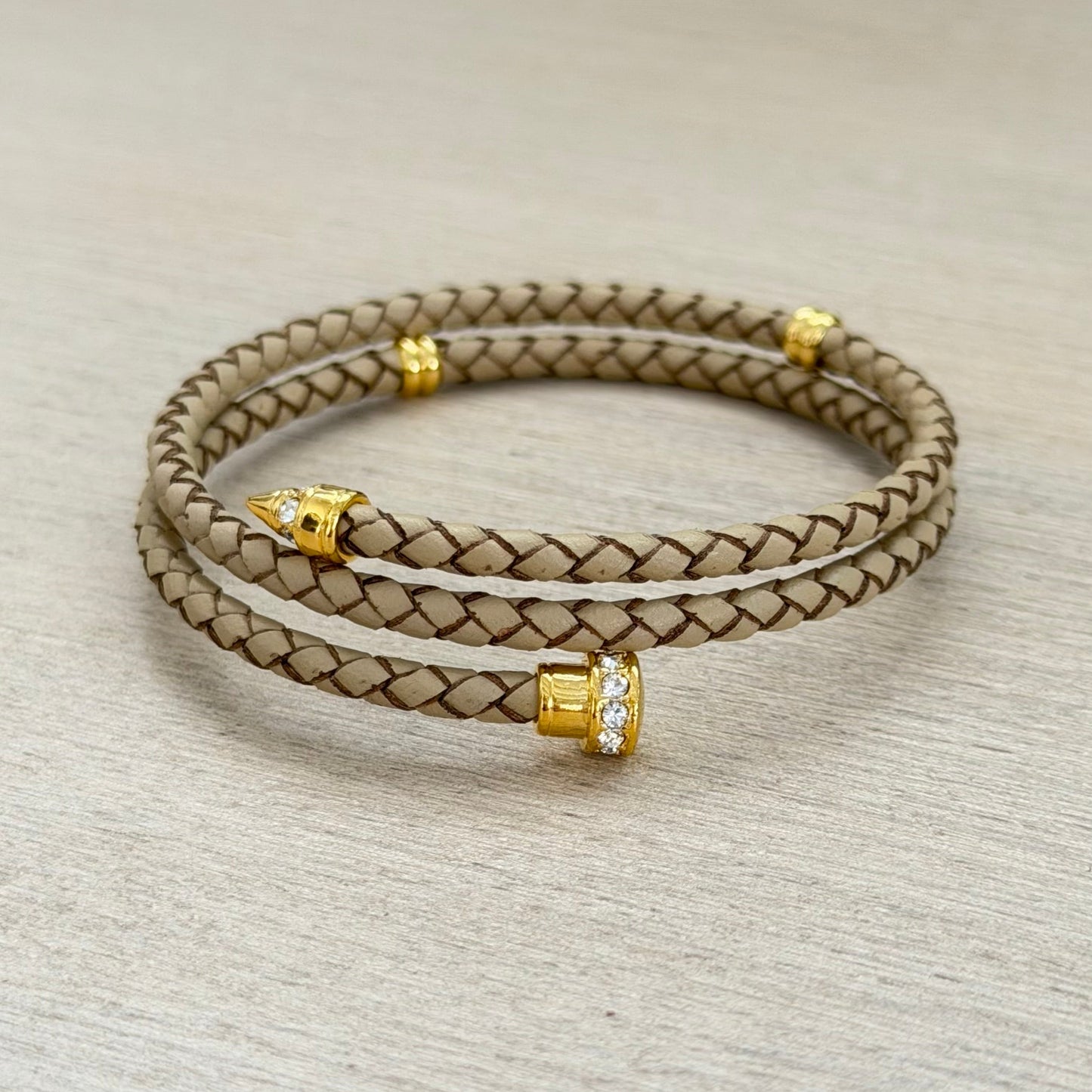 Braided leather bracelet with gold accents on a light gray background