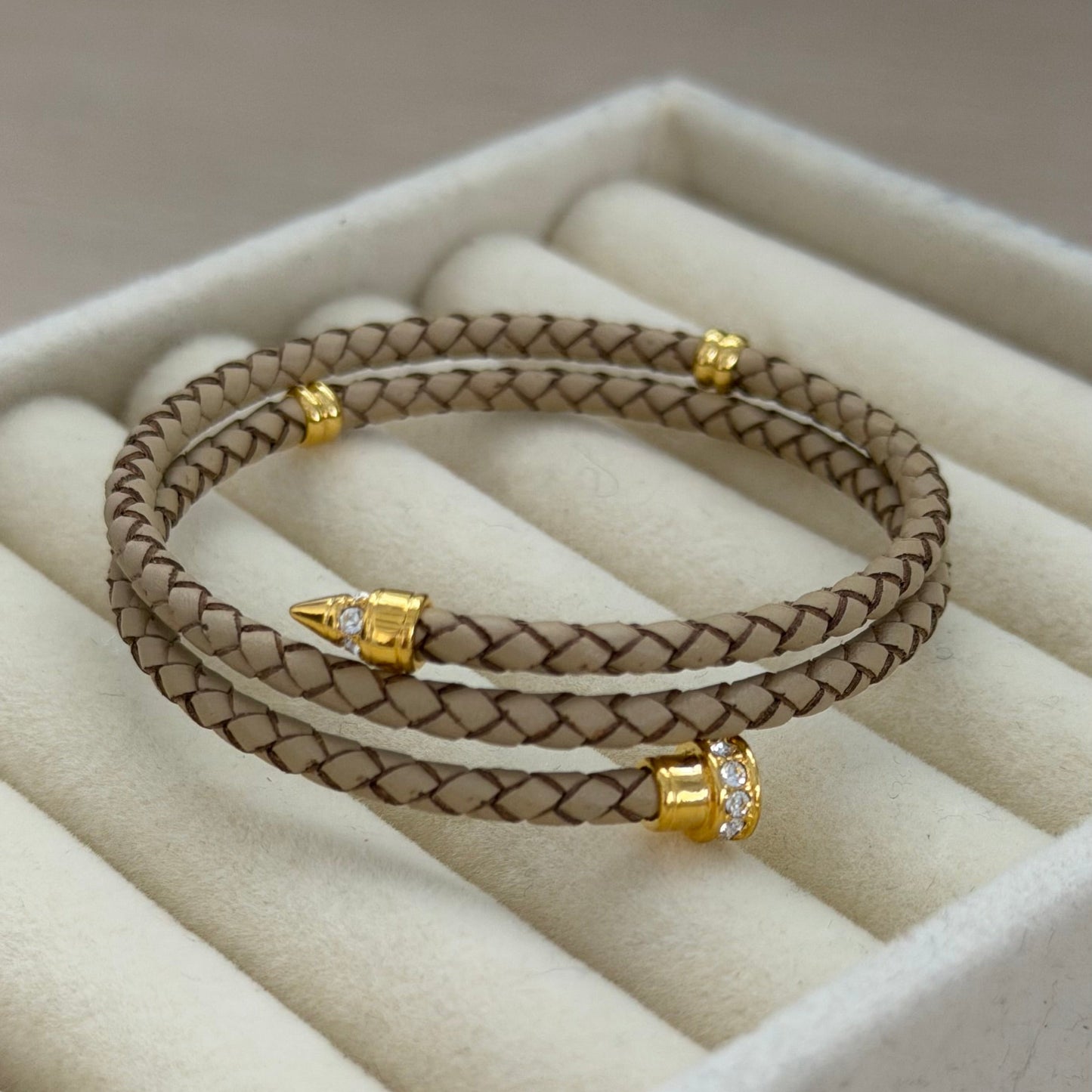 Beige braided bracelet with gold accents on a beige cushioned surface