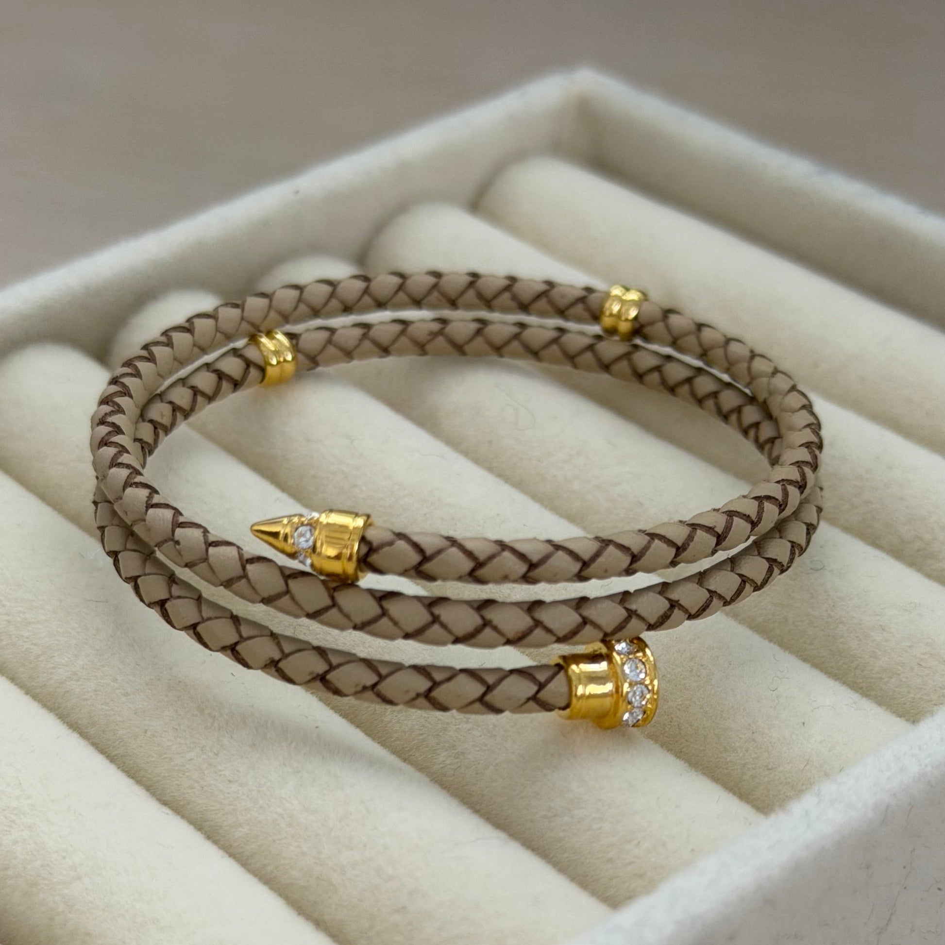 Beige braided bracelet with gold accents on a beige cushioned surface