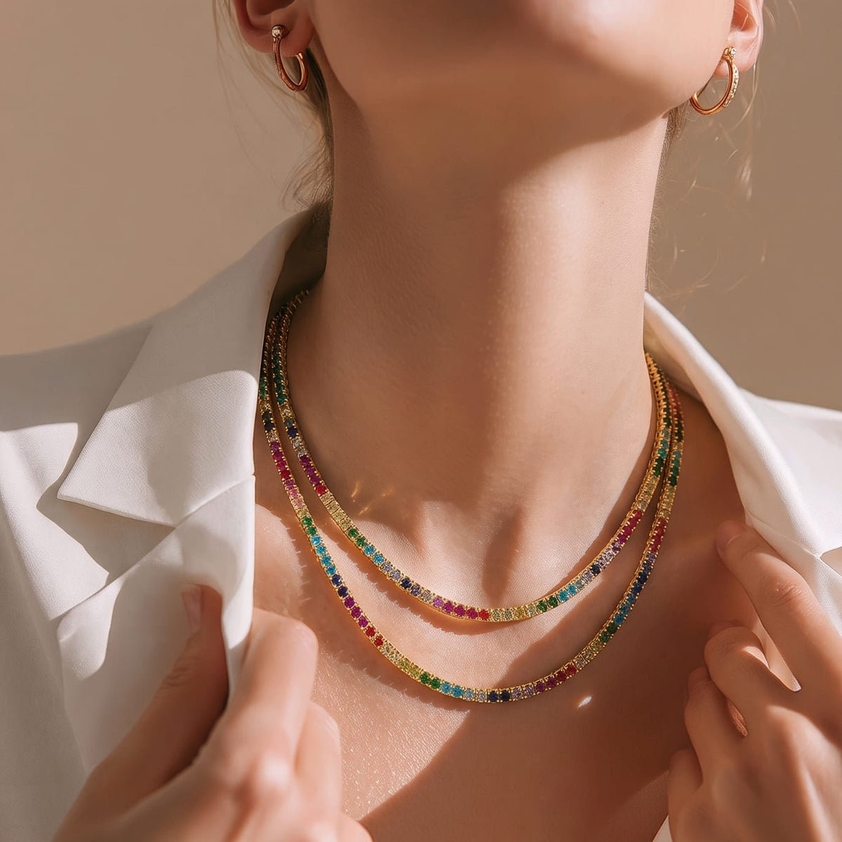 A close-up lifestyle shot of a model wearing a multi-strand beaded necklace with colorful round beads, styled with gold hoop earrings and a white blazer.