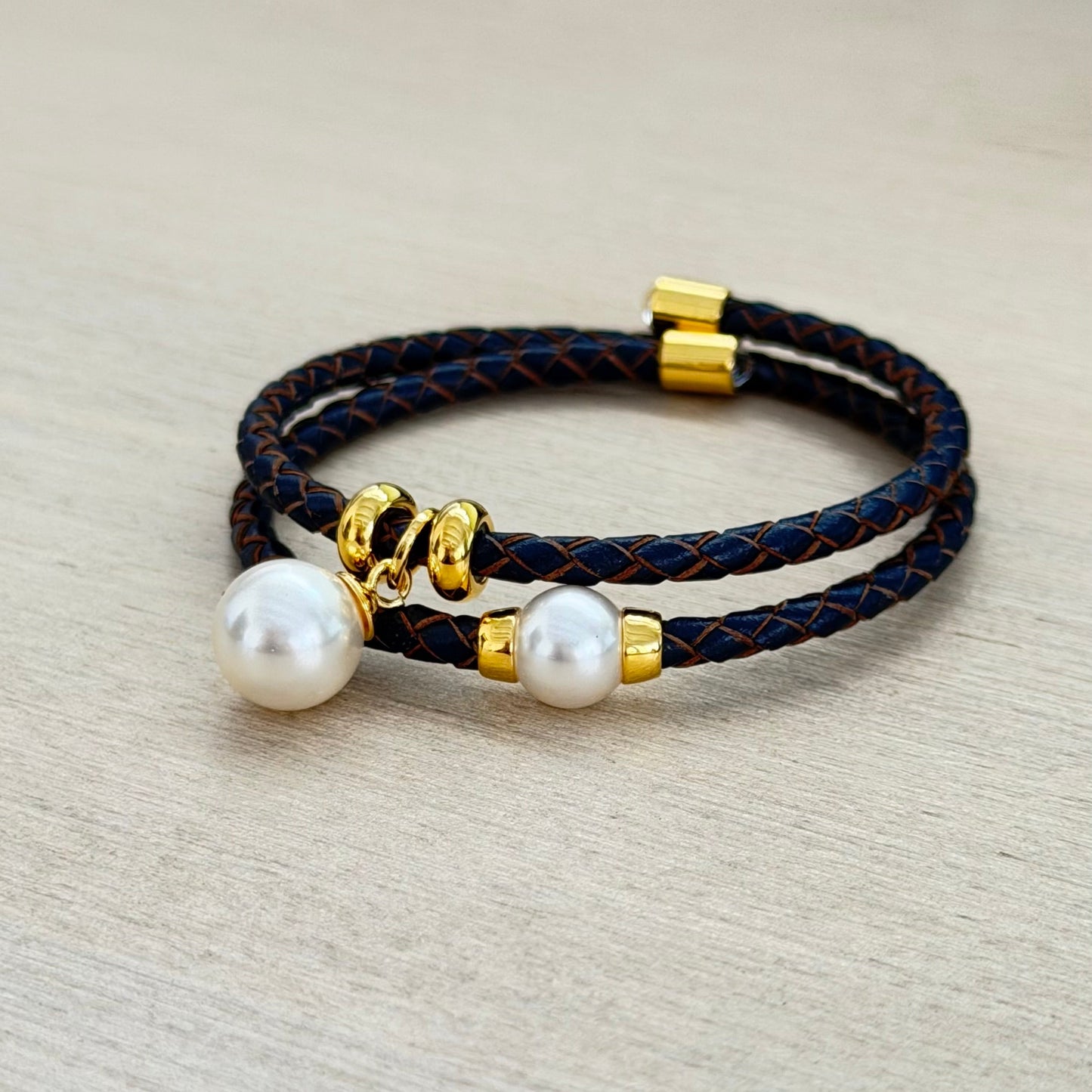 Black braided bracelet with pearls and gold accents on a beige background