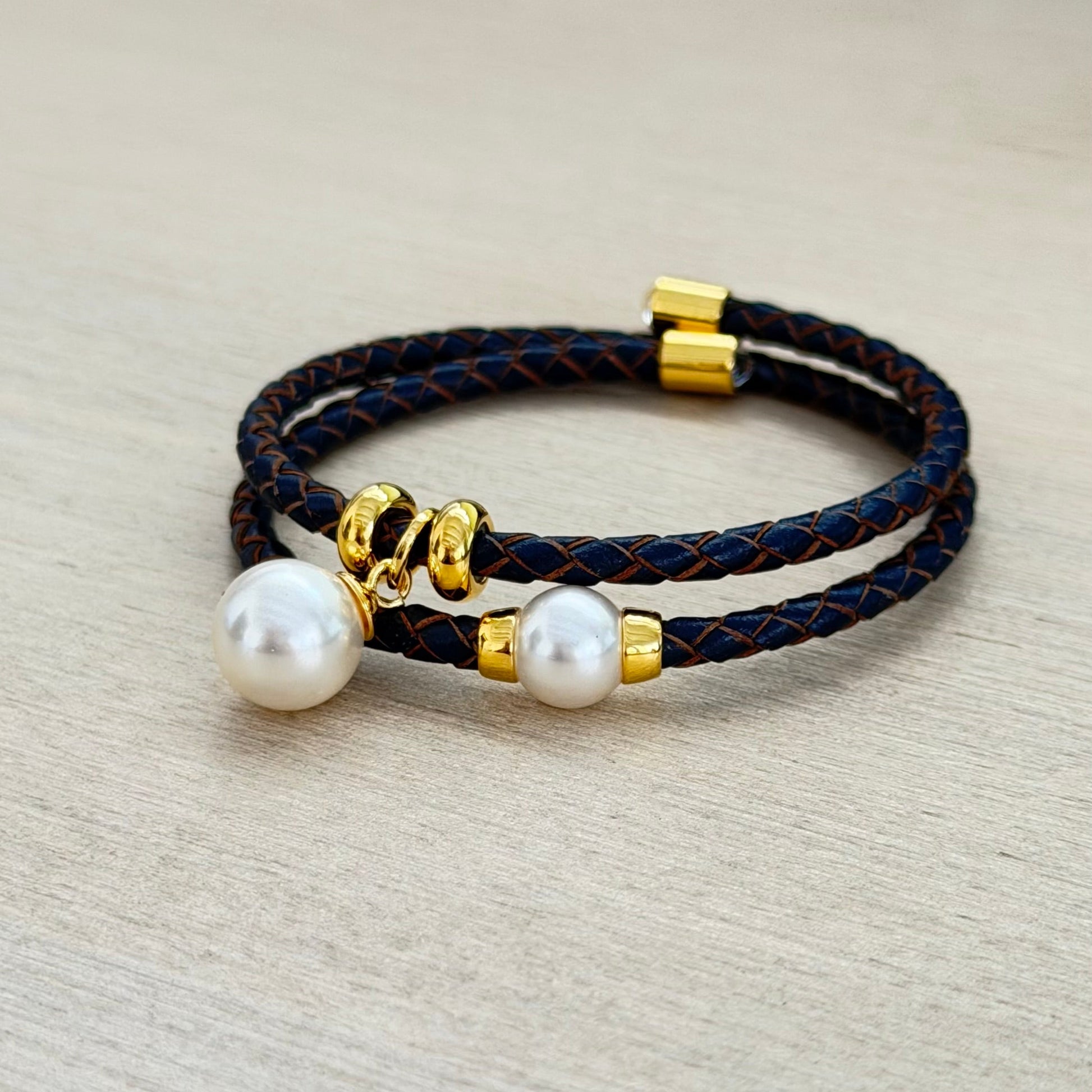 Black braided bracelet with pearls and gold accents on a beige background