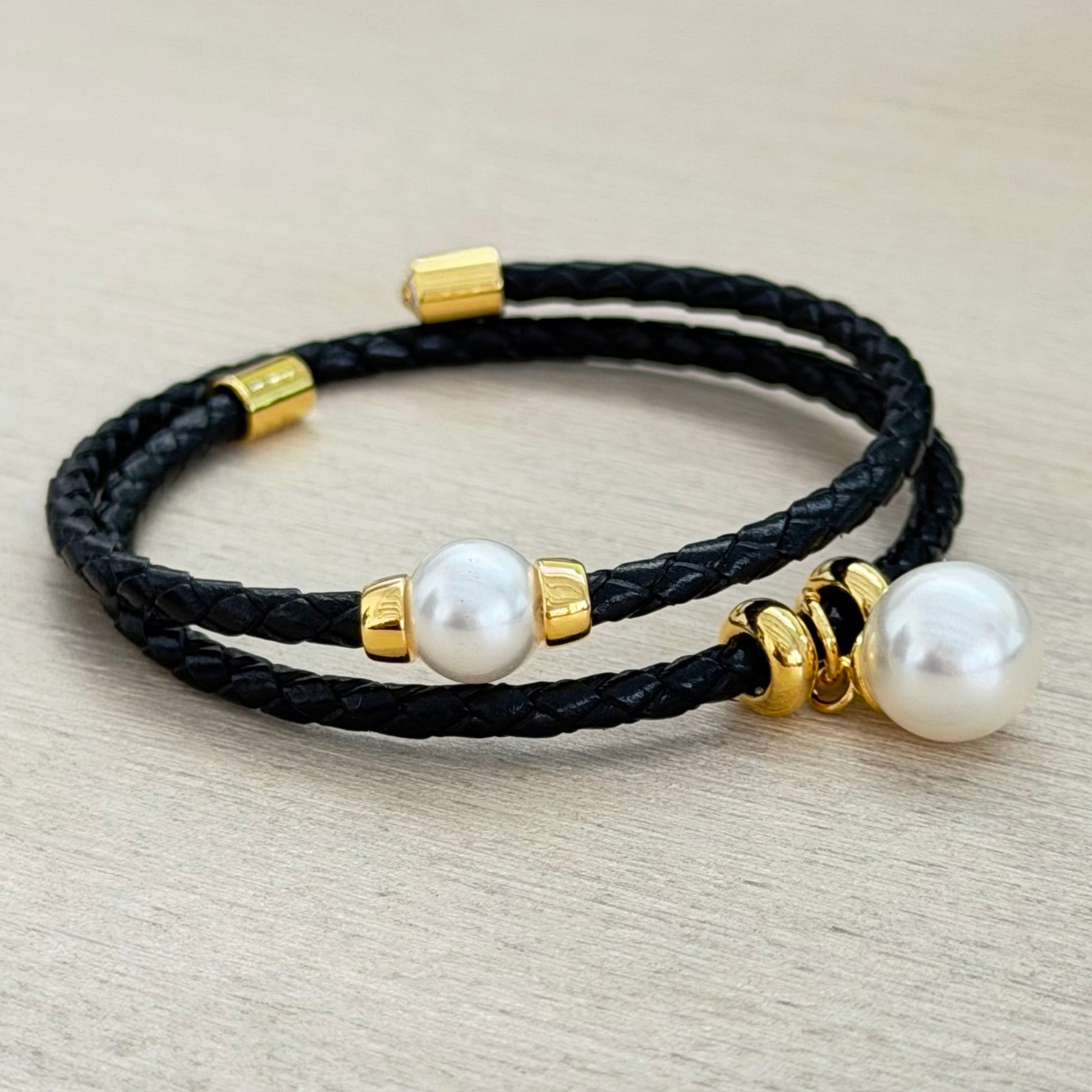 Black leather bracelet with gold accents and white pearls on a light gray surface