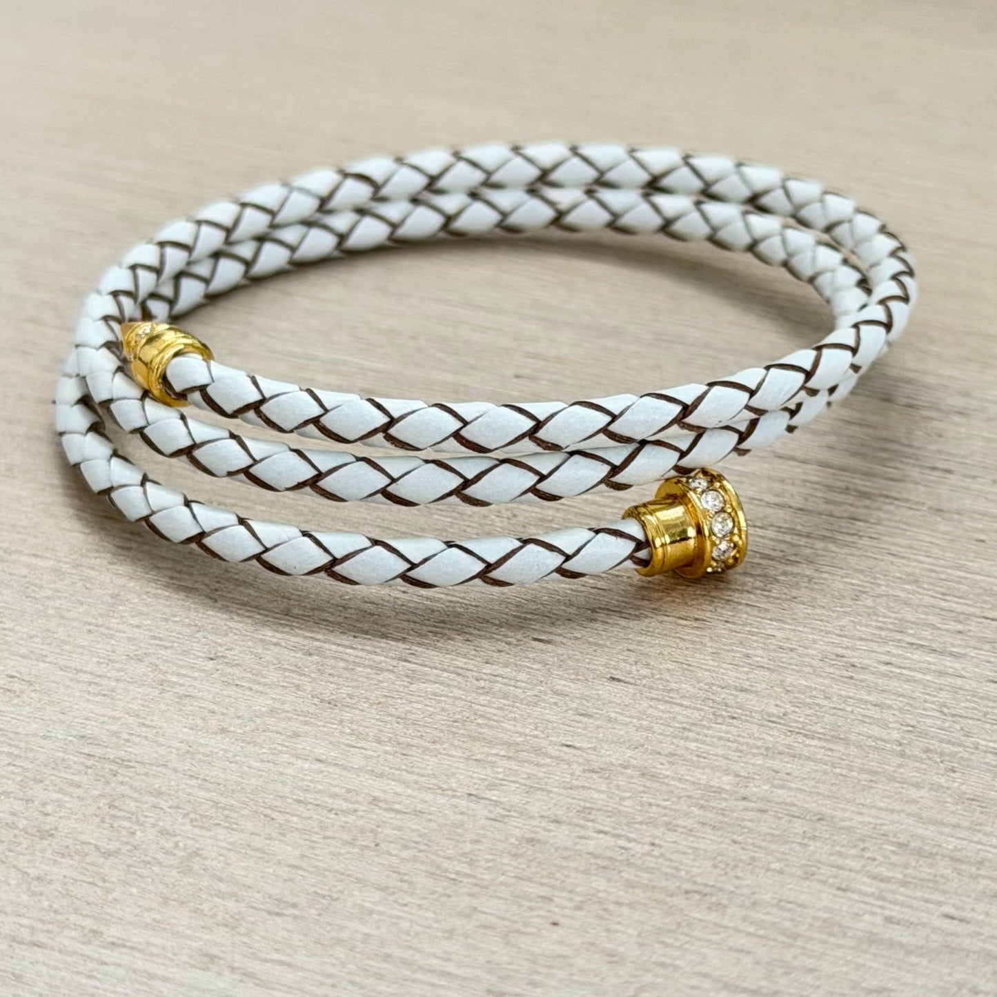 White braided leather bracelet with gold beads on a beige surface