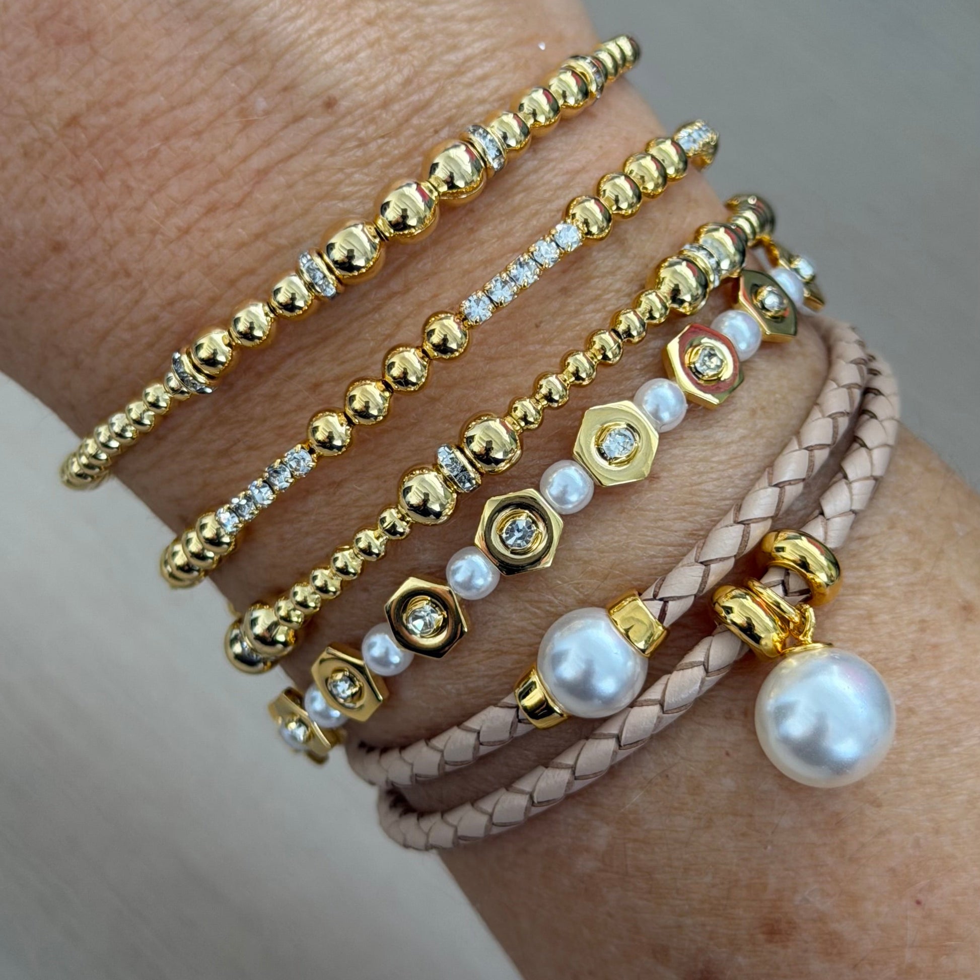 Close-up of a wrist wearing multiple gold and pearl bracelets on a neutral background