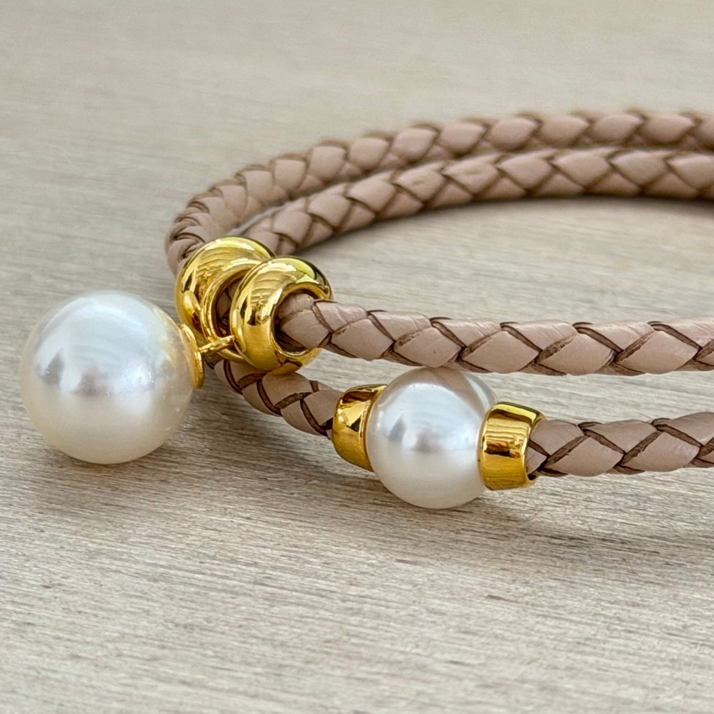 Bracelet with braided leather cord and pearl beads on a light wooden surface